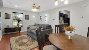 A modern living room with a gray sofa, a wooden dining table, and a ceiling fan.
