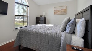 A bedroom with a bed, a dresser, a window with blinds, a ceiling fan, and a painting on the wall.