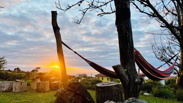 A hammock tied between two trees in a grassy area with a sunset in the background. - Biscoitos Top View apartment overlooking the sea with AC and very fast Wi-Fi (Biscoitos)