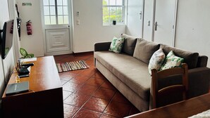 A furnished room with a sofa, a desk with a laptop, a fire extinguisher, and a window. - Biscoitos Top View apartment overlooking the sea with AC and very fast Wi-Fi (Biscoitos)