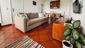 A living room with a sofa, a dining table, chairs, a TV, and a potted plant. - Biscoitos Top View apartment overlooking the sea with AC and very fast Wi-Fi (Biscoitos)