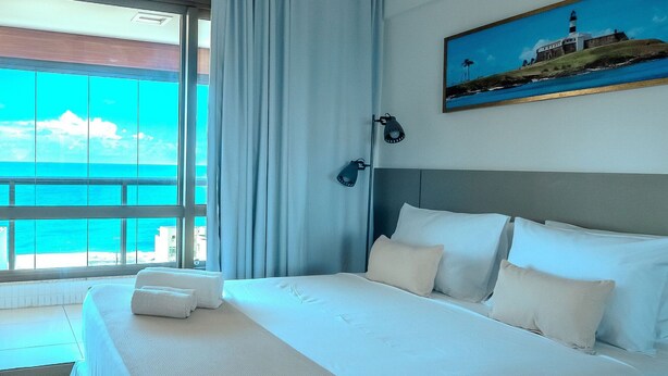 A hotel room with a large bed, a painting of a lighthouse, and a view of the ocean through the window.