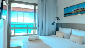 A hotel room with a large bed, a view of the ocean, and a painting of a lighthouse.