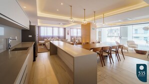 A modern kitchen with a central island, dining area with wooden chairs, and a large window providing natural light.