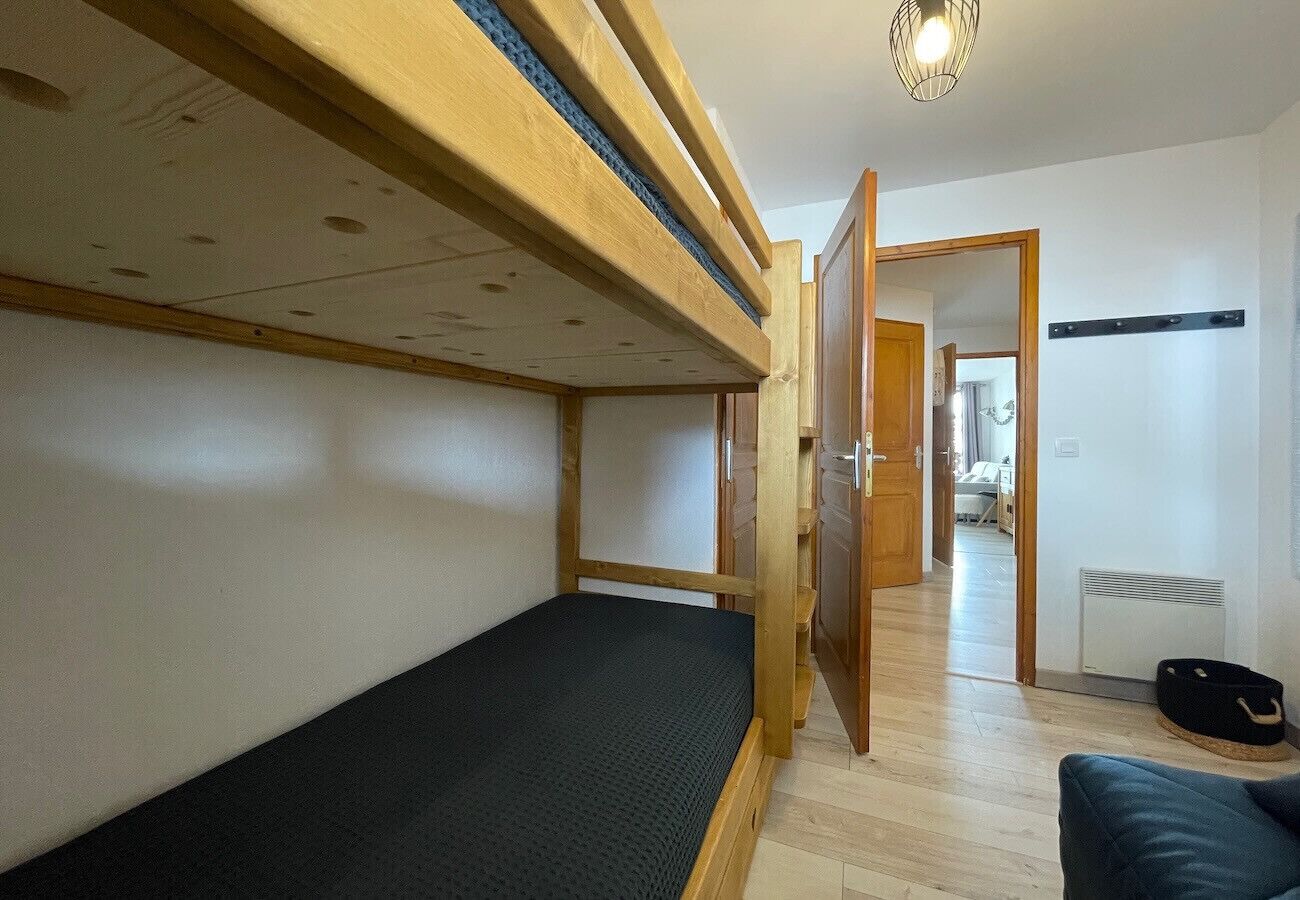 Une pièce avec un lit superposé, une porte donnant sur une autre pièce, un radiateur et un sac posé sur le sol.