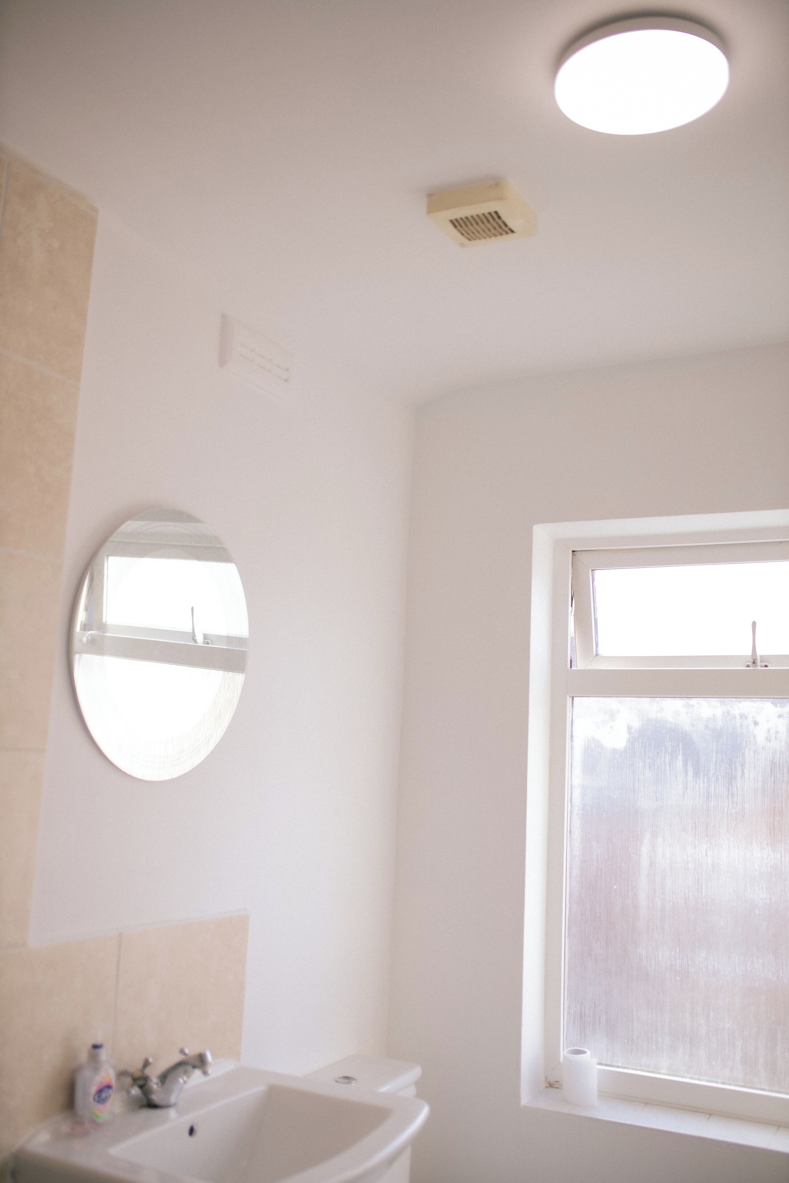 A bathroom with a sink, mirror, window, and ceiling light.