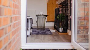 A narrow entrance with a glass door leading to a room with a wooden door, a small table with a chair, and a potted plant.