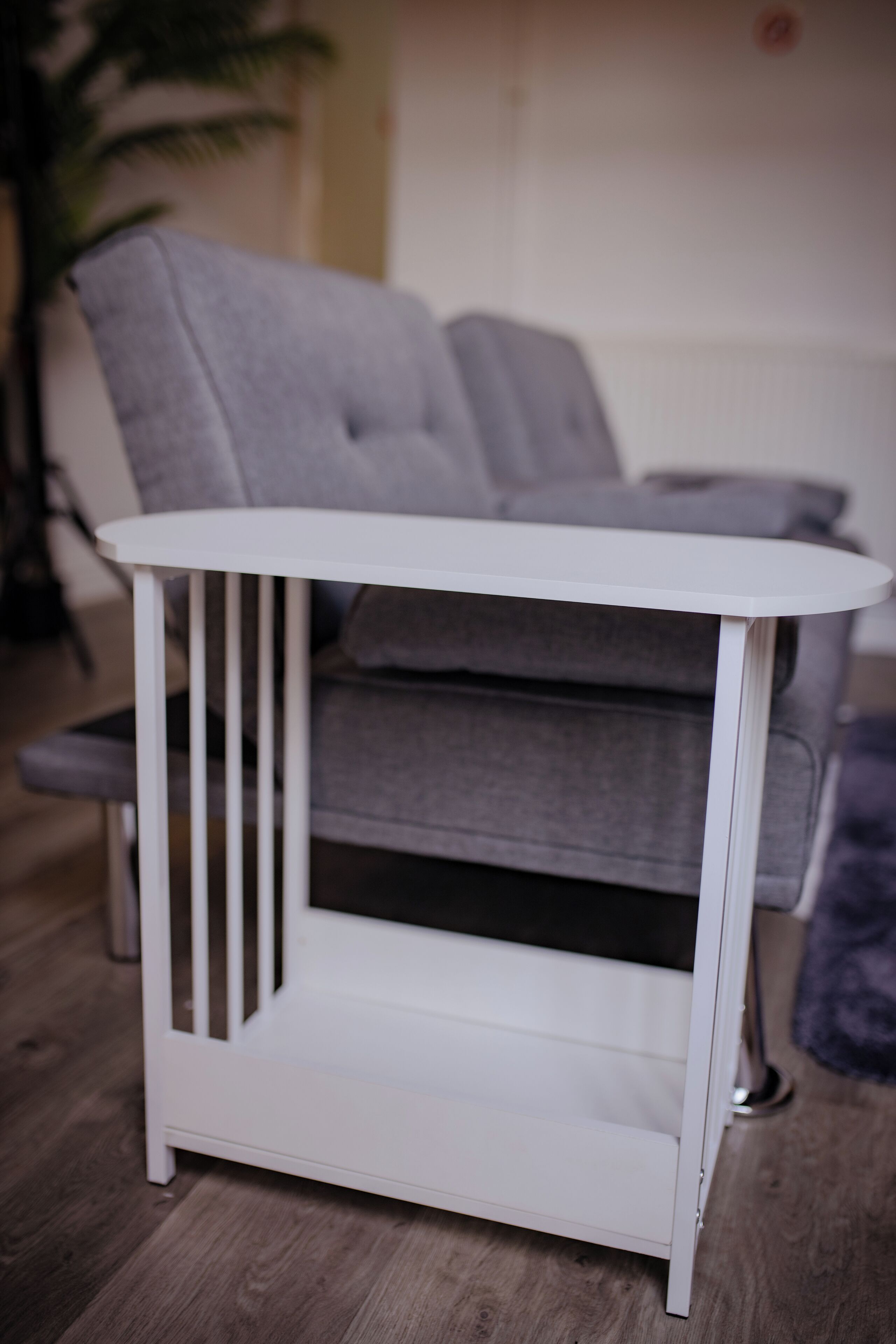 Una mesa blanca con listones verticales, ubicada frente a un sofá gris en una habitación con suelo de madera.