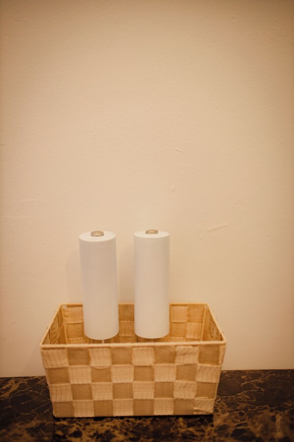 A checkered basket containing two rolls of white toilet paper on a dark marble countertop against a plain wall.