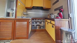 Une cuisine de taille réduite, avec des meubles en bois, une hotte en acier inoxydable et un appareil électroménager rouge posé sur le plan de travail.