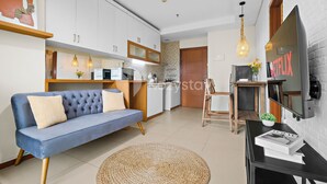 Una sala de estar moderna con un sofá, un televisor y una cocina al fondo.