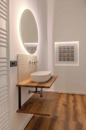 A modern bathroom with a round mirror, a wooden vanity, and a decorative tile backsplash.