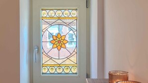 Une porte ornée de vitraux, une petite marche menant à cette porte, et trois bougies posées sur une étagère en bois à côté de la porte.