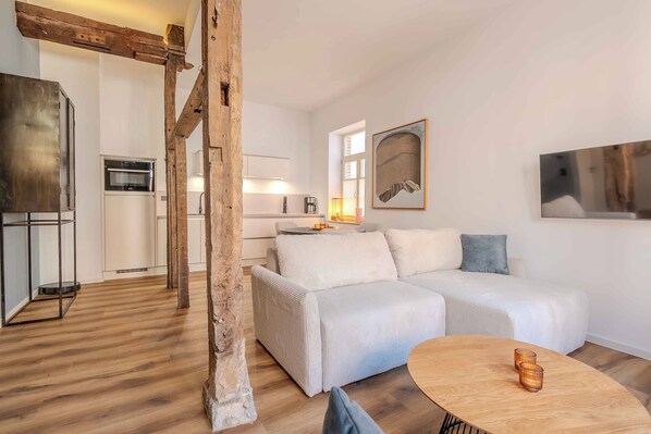 A modern living room with a wooden floor, white sofa, and a round wooden table.