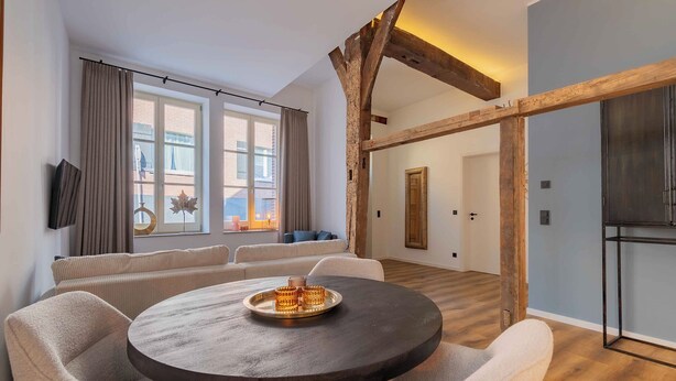 Un salon moderne avec une table ronde, des canapés de couleur beige et une structure en poutres apparentes.
