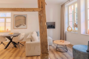 A modern living room with a wooden beam structure, a round dining table, a sofa, and a TV mounted on the wall.