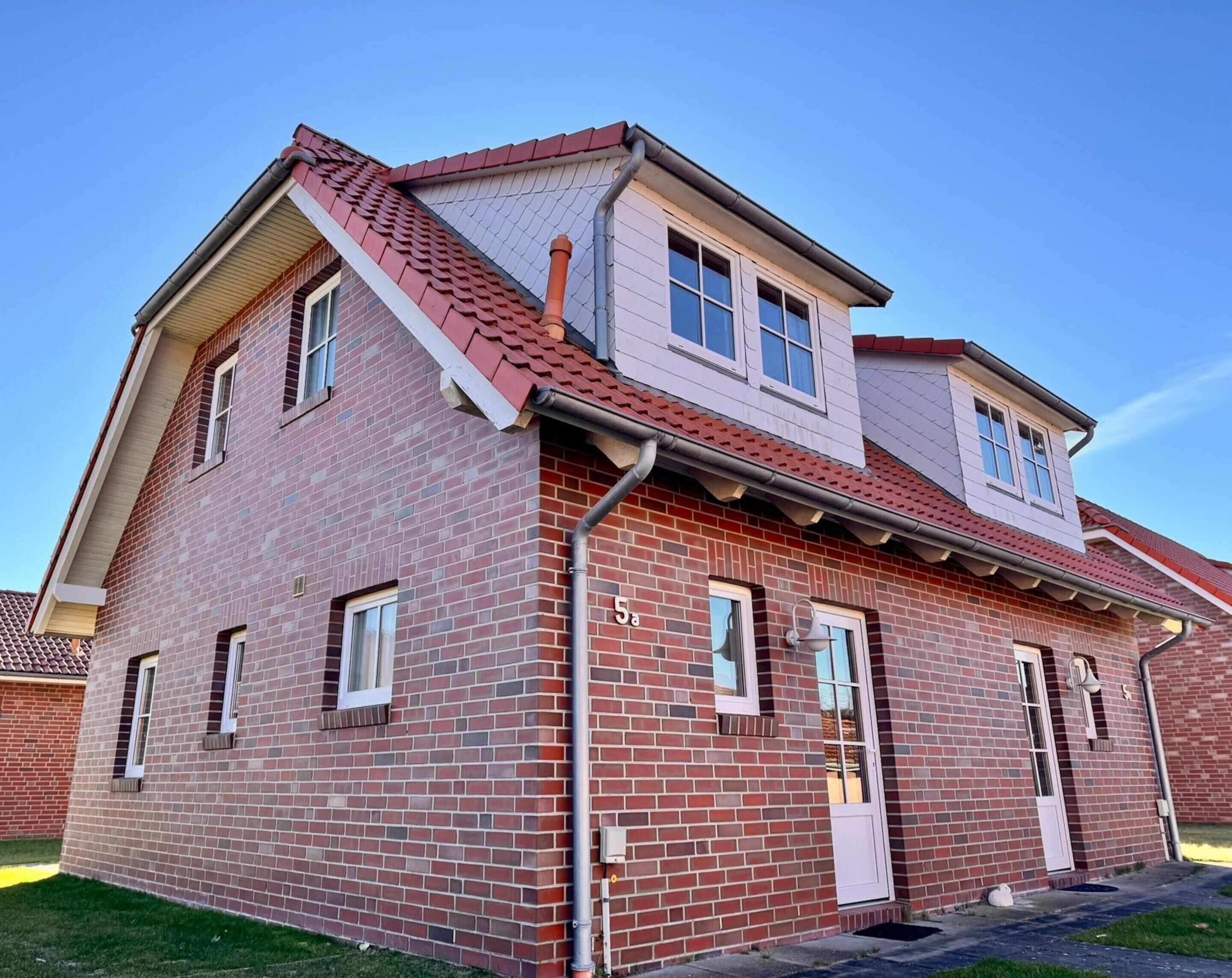 A two-story brick building with a red-tiled roof, multiple windows, and a visible door.