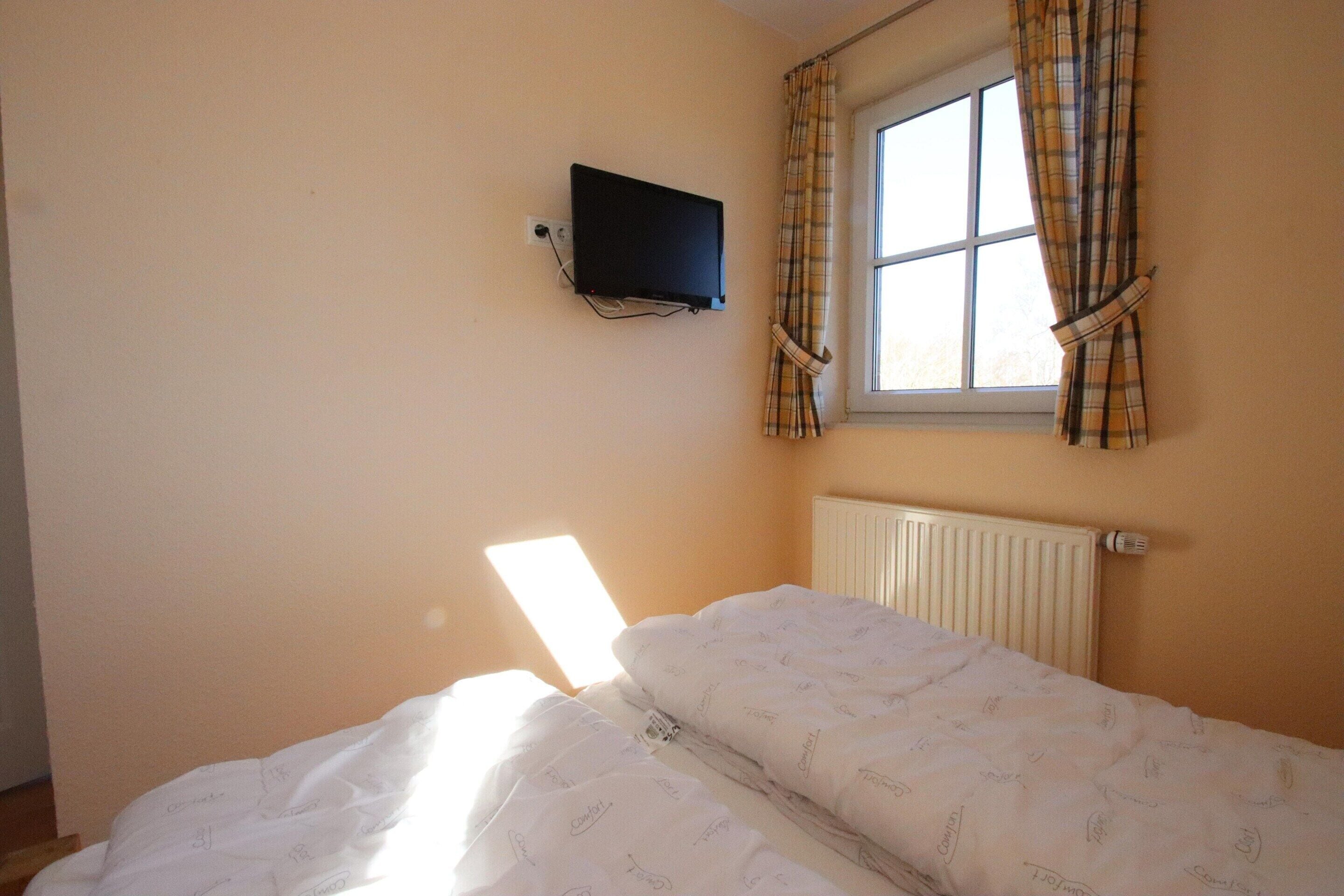 A bedroom with a bed, a television mounted on the wall, and a window with curtains.