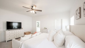 A bedroom with a bed, a TV, a dresser, a ceiling fan, and a door.
