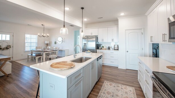 A modern kitchen with white cabinetry, a central island, stainless steel appliances, and pendant lighting.