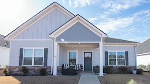 A two-story house with a front porch, a door with a wreath, and a small seating area with chairs and a table.