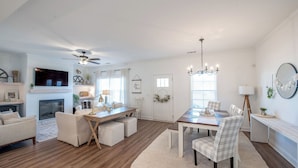 A spacious living room with a fireplace, a dining area with a table and chairs, and a television mounted on the wall.