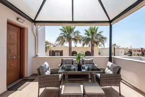 An outdoor balcony with a glass table and wicker furniture, overlooking palm trees and buildings. - Solsalt 1min Walk to Beach 1min From Everything (Platanias)