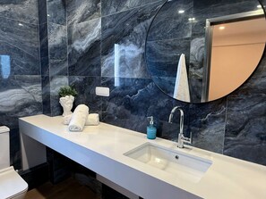 A modern bathroom with a marble backsplash, a white sink, and a round mirror. - Solsalt 1min Walk to Beach 1min From Everything (Platanias)