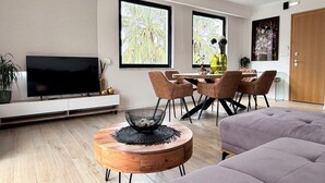 A modern living room with a flat-screen TV, a round wooden coffee table, a sofa, and a dining area with a table and chairs. - Solsalt 1min Walk to Beach 1min From Everything (Platanias)