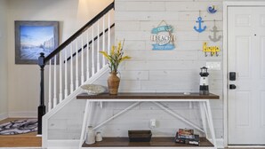 Eine Treppe mit weißer Reling, eine hölzerne Bank mit einem Blumenstrauß aus gelben Blumen und ein kleines Regal mit Büchern und einem Leuchtturm-Modell.