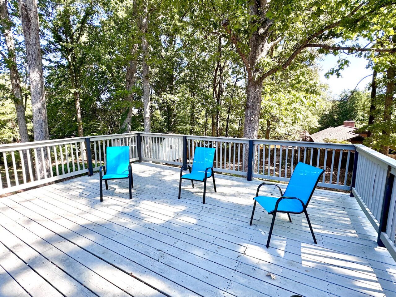 A wooden deck with three blue chairs and a white railing.