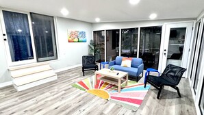 A modern living room with a wooden floor, a blue sofa, a coffee table, and black chairs.