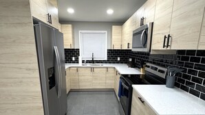 A modern kitchen with light wood cabinets, a stainless steel refrigerator, a microwave, and a dishwasher.