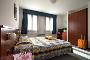 Une chambre d’hôtel avec un lit, un bureau, une armoire et une valise.