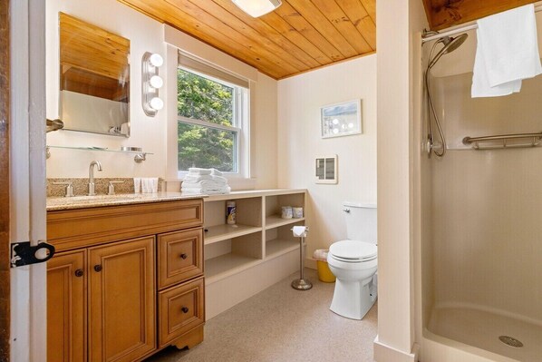 Ein Badezimmer mit Holzwaschtisch, Fenster, Dusche und Toilette.