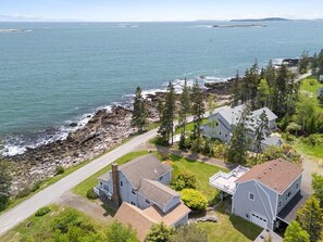 A coastal residential area with houses, a rocky shoreline, and a view of the ocean.