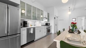 A modern kitchen with stainless steel appliances, white cabinetry, and a dining area with a table set for two.