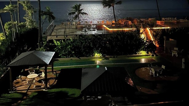 Een nachtzicht van een resort met een zwembad, palmbomen en uitzicht op de oceaan.