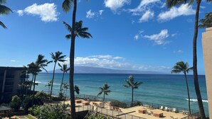 Een balkon met uitzicht op de oceaan, palmbomen en een gebouw op de achtergrond.