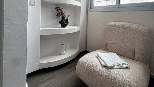 A room with a white curved shelving unit, a beige armchair, and a window with blinds. - Degn'An Holding Residence. (Abidjan)