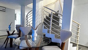 A modern interior with a glass table surrounded by cushioned chairs, a spiral staircase, and a minimalist design. - Degn'An Holding Residence. (Abidjan)