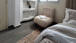 A bedroom with a bed, a chair, a shelf unit, and a window. - Degn'An Holding Residence. (Abidjan)
