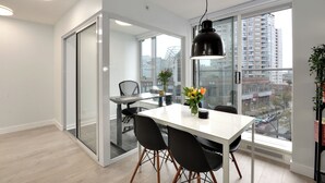 Un espace repas moderne avec une table blanche, des chaises noires et un luminaire suspendu noir.