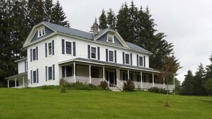 A large, two-story white house with a covered porch and a grassy yard.