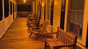 A covered porch with wooden benches and columns, a railing, and evenly spaced windows.