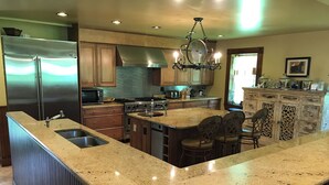 A kitchen with a stainless steel refrigerator, a microwave, a stove, and a sink. There is a chandelier hanging above the island with bar stools.