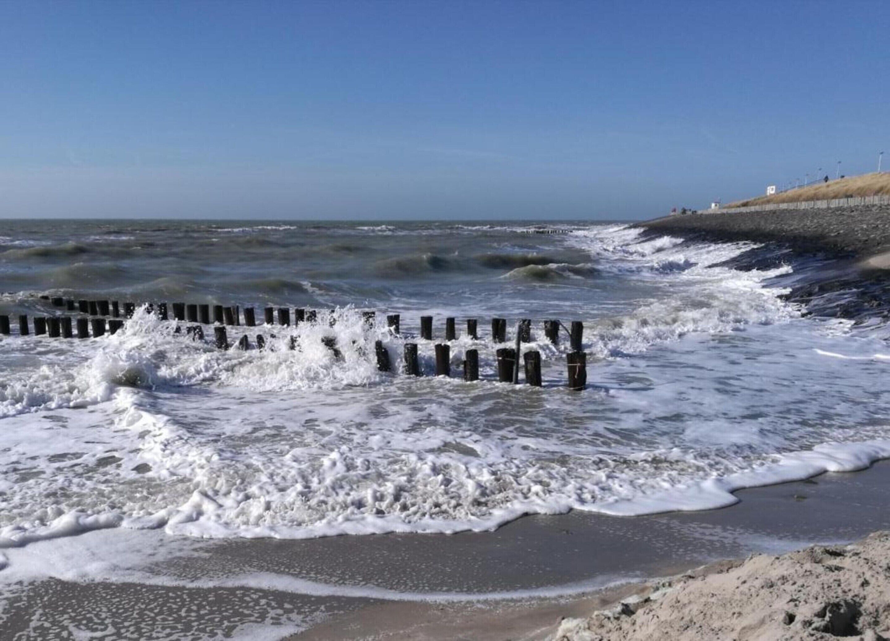 Una playa con olas rompiendo contra un espigón de madera.