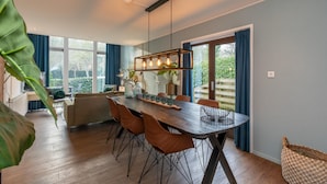 A dining area with a wooden table, orange chairs, and a hanging light fixture. - Holiday Home in Zeeland Near the Beach (Biggekerke)