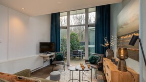 A modern living room with a television, seating area, and a view of the outdoors. - Holiday Home in Zeeland Near the Beach (Biggekerke)