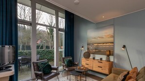 A modern living room with a large window, a television, a sofa, a coffee table, and a cabinet. - Holiday Home in Zeeland Near the Beach (Biggekerke)